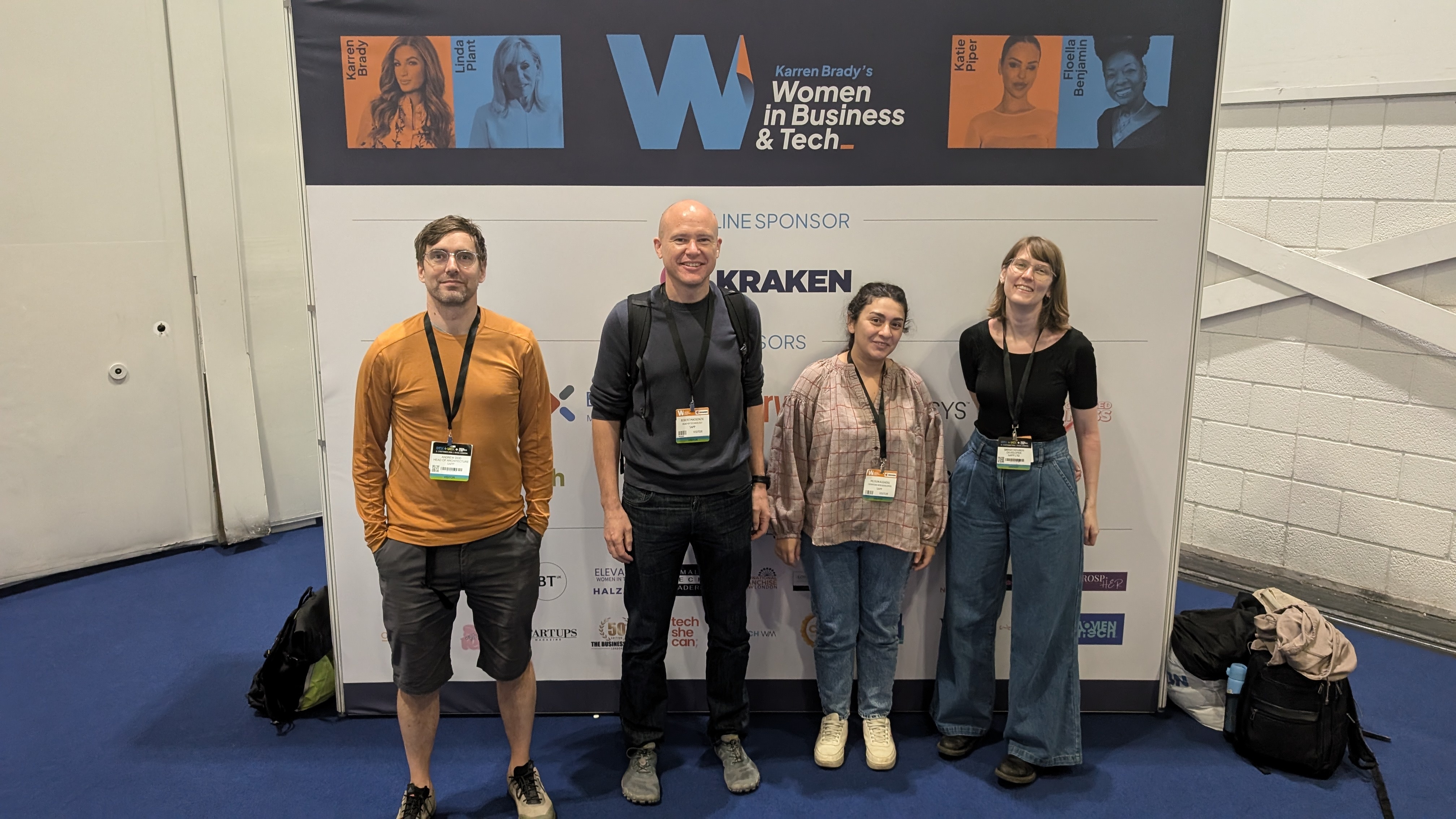 The developer team (left to right, Andrew, Rob, Mejsun, Sarah) standing in front of a &quot;Karren Brady’s Women in Business &amp; Tech Expo&quot; poster